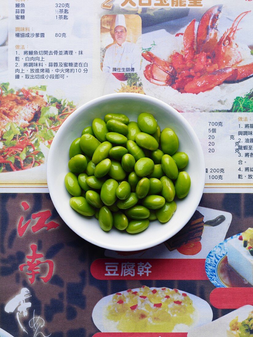 Edamame beans in a white dish on japanese newspaper