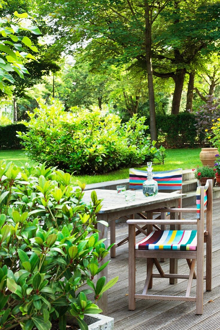 Regiestühle mit bunten Streifen und Tisch auf Holzterrasse im Garten