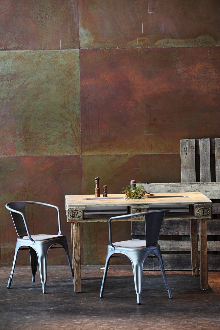 Rustic dining table made from pallet and metal chairs against corten steel wall