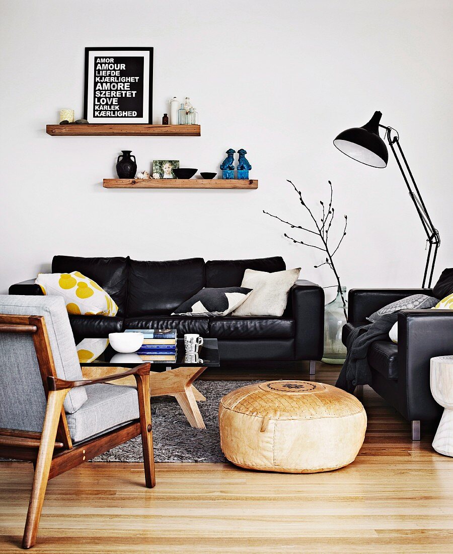 Pouffe between fifties-style armchair and leather sofa set and black, metal standard lamp in living room