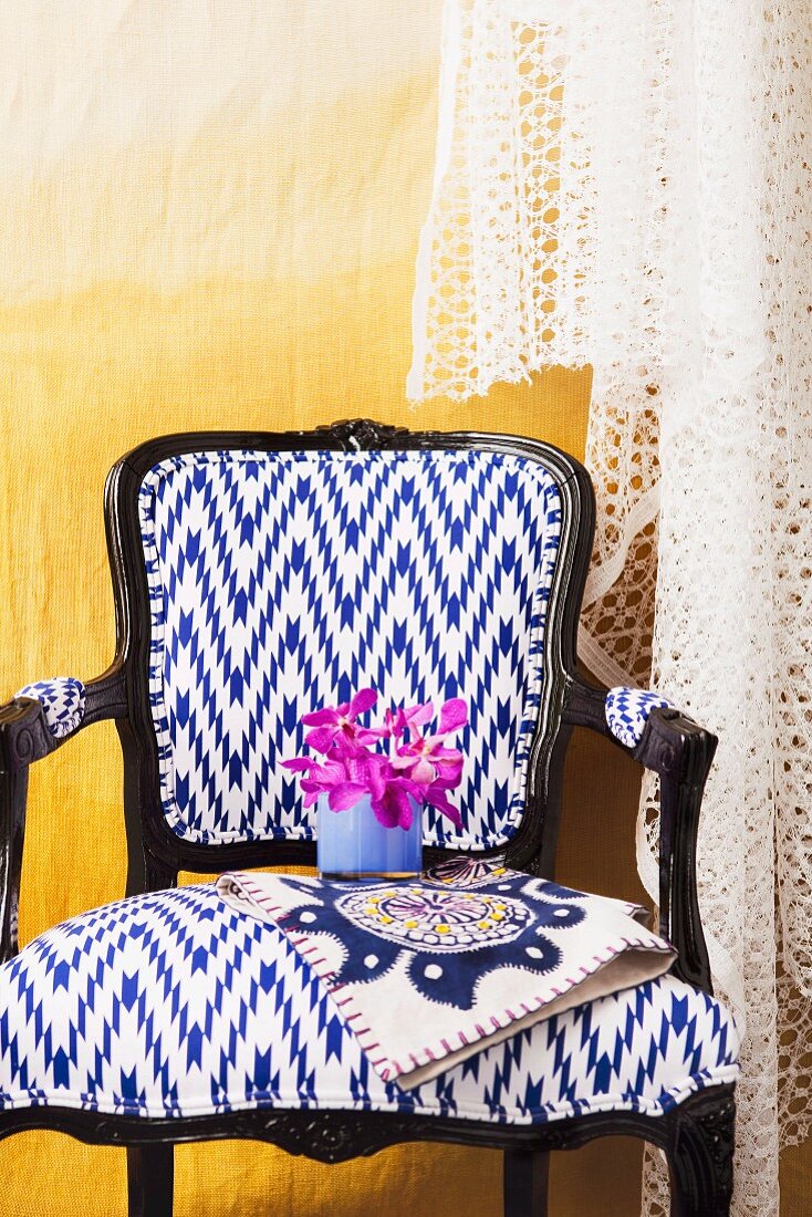 Postmodern chair with white and blue upholstery and black wooden frame against yellow wall draped in lace fabric