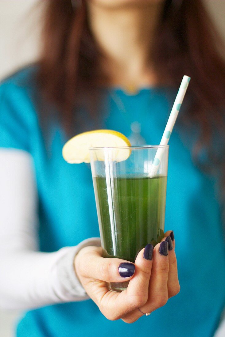 A woman holding a glass of apple juice with chlorella (freshwater algae)