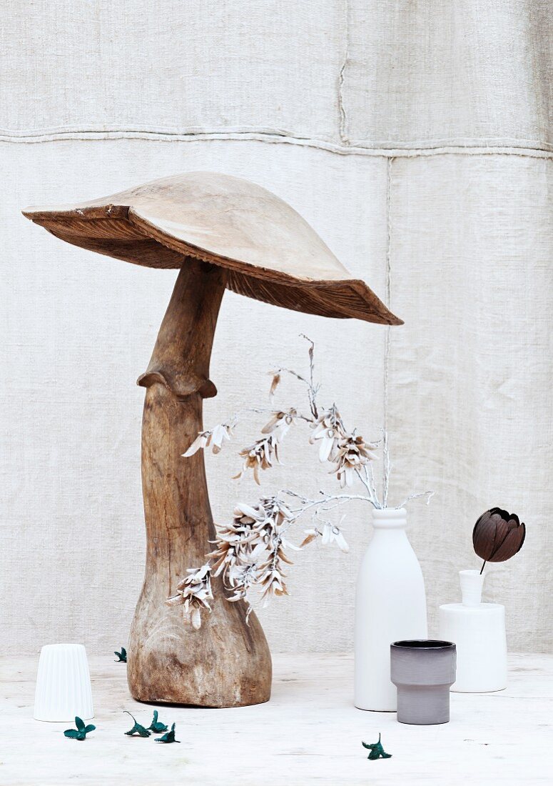 Grosser Deko-Pilz aus Holz und eingefärbte Pflanzen in Vasen