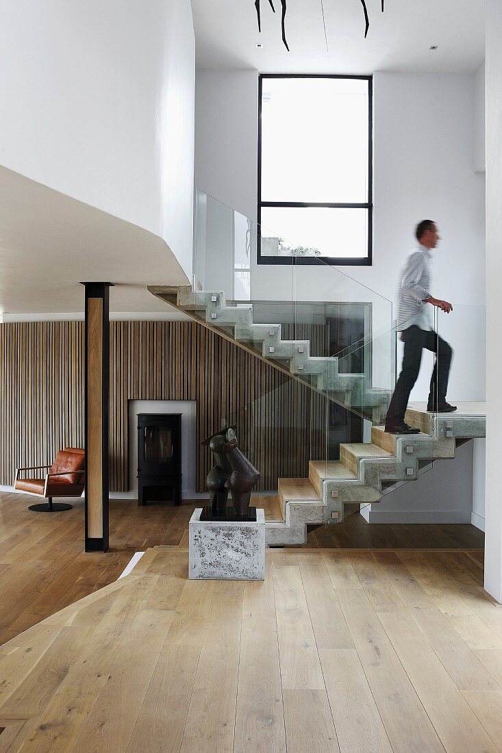 Open-plan stairwell in contemporary house with sculpture on plinth in front of staircase and man walking up stairs