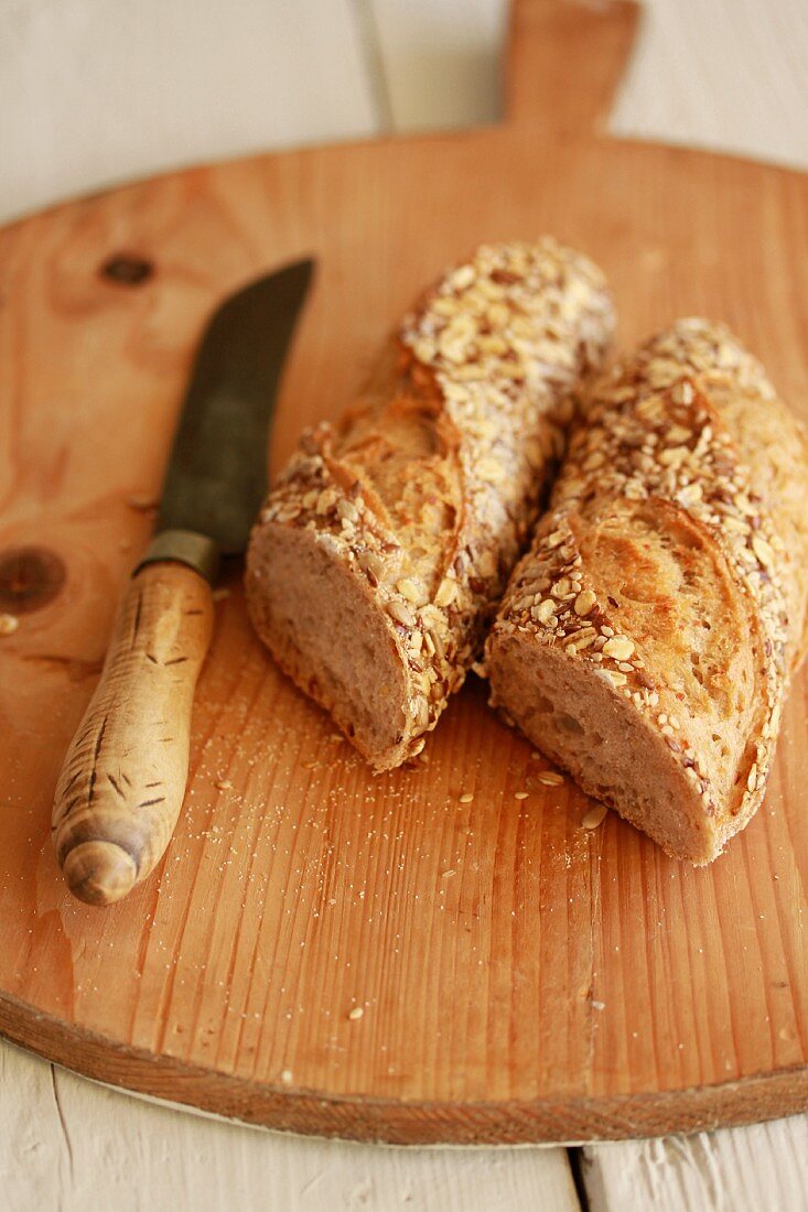 Halved wholegrain baguette with a knife on a wooden board