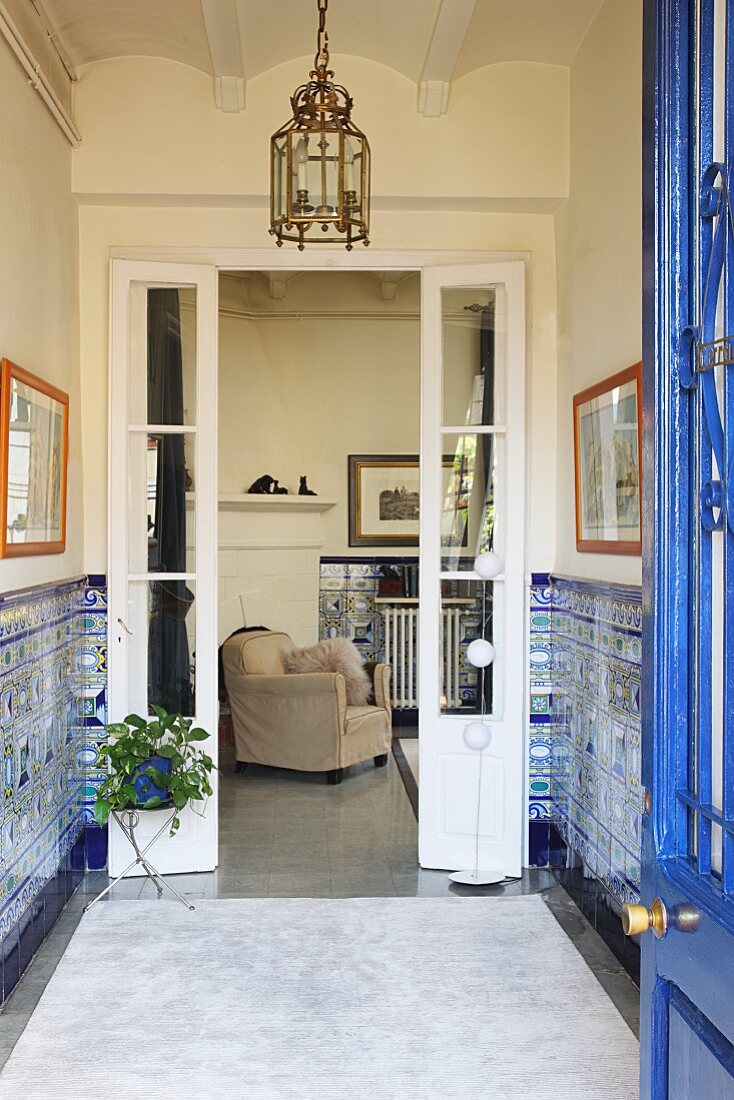 View through open door into foyer with half-height tiled walls and pale grey rug in front of open double doors showing view of armchair beyond