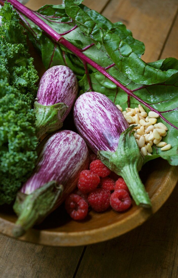 Striped aubergines, raspberries, salad and pine nuts in a wooden bowl