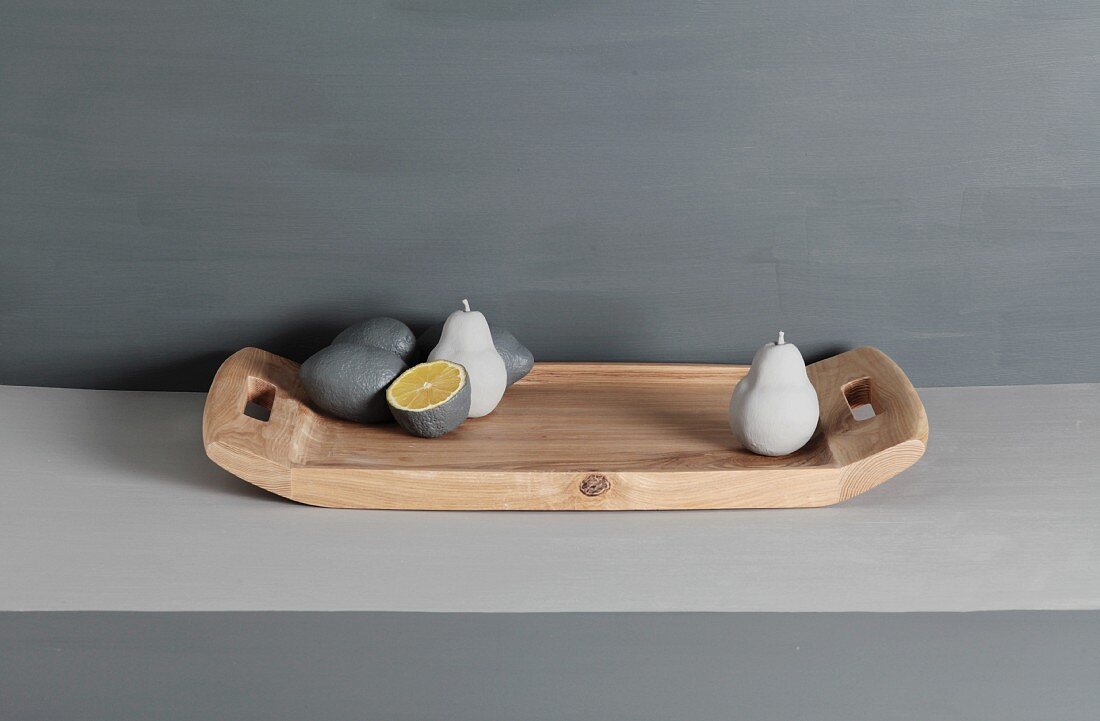 Grey lemon and pear sculptures on wooden tray against grey-painted background