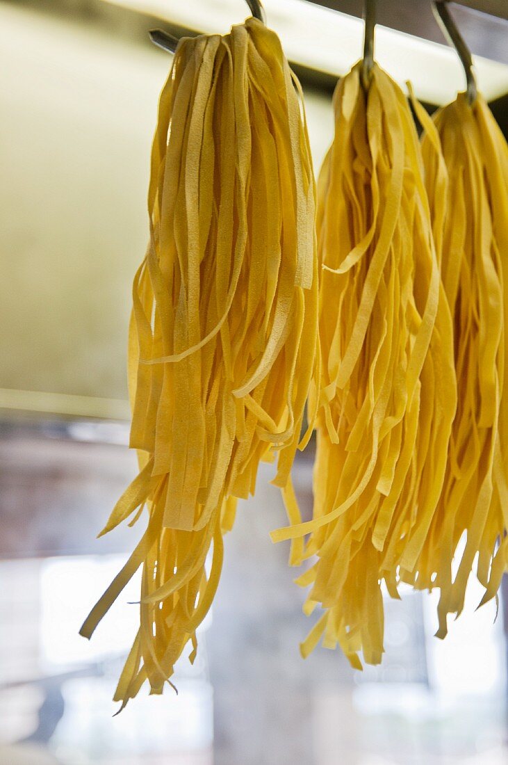 Bunches of tagliatelle hung up on large hooks to dry