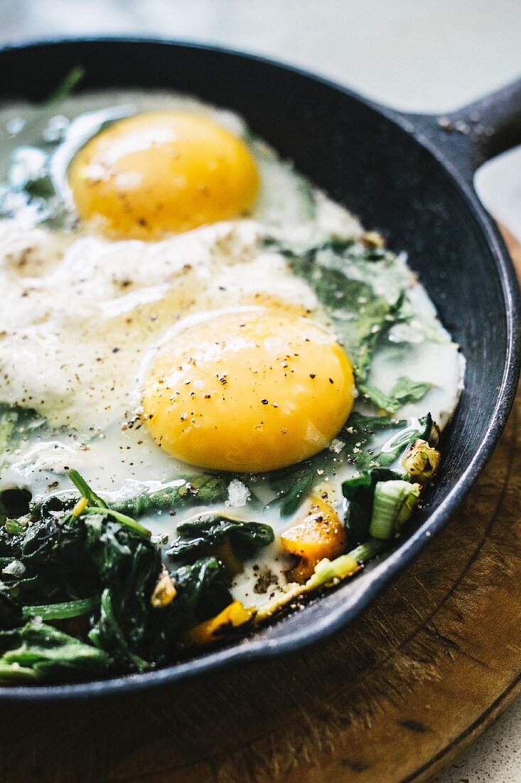 Fried eggs with spinach and spring onions in a frying pan