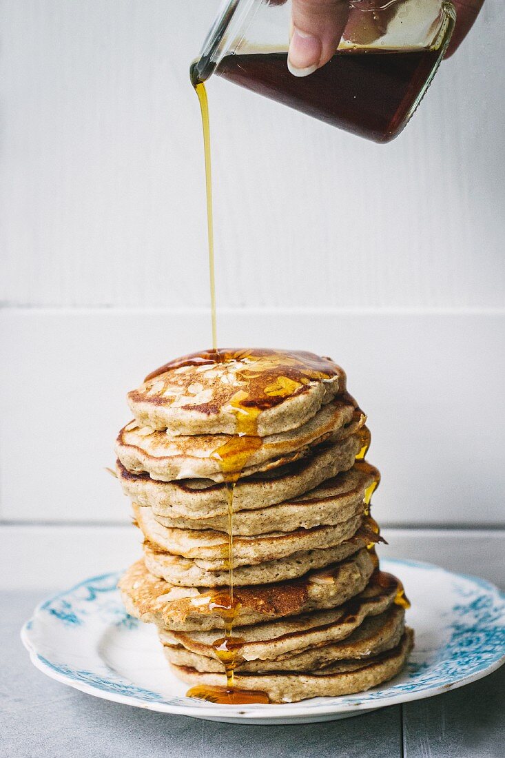 A hand pouring honey over a stack of pancakes