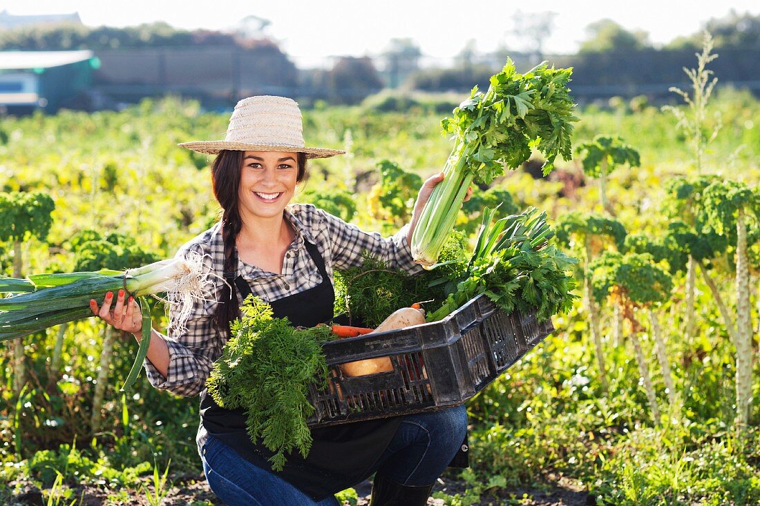A young woman proudly holding up freshly harvested vegetables in the field