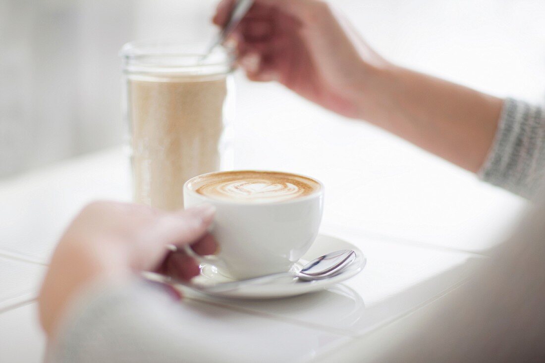 Frau mit Tasse Kaffee & Zuckerglas am Tisch eines Cafes