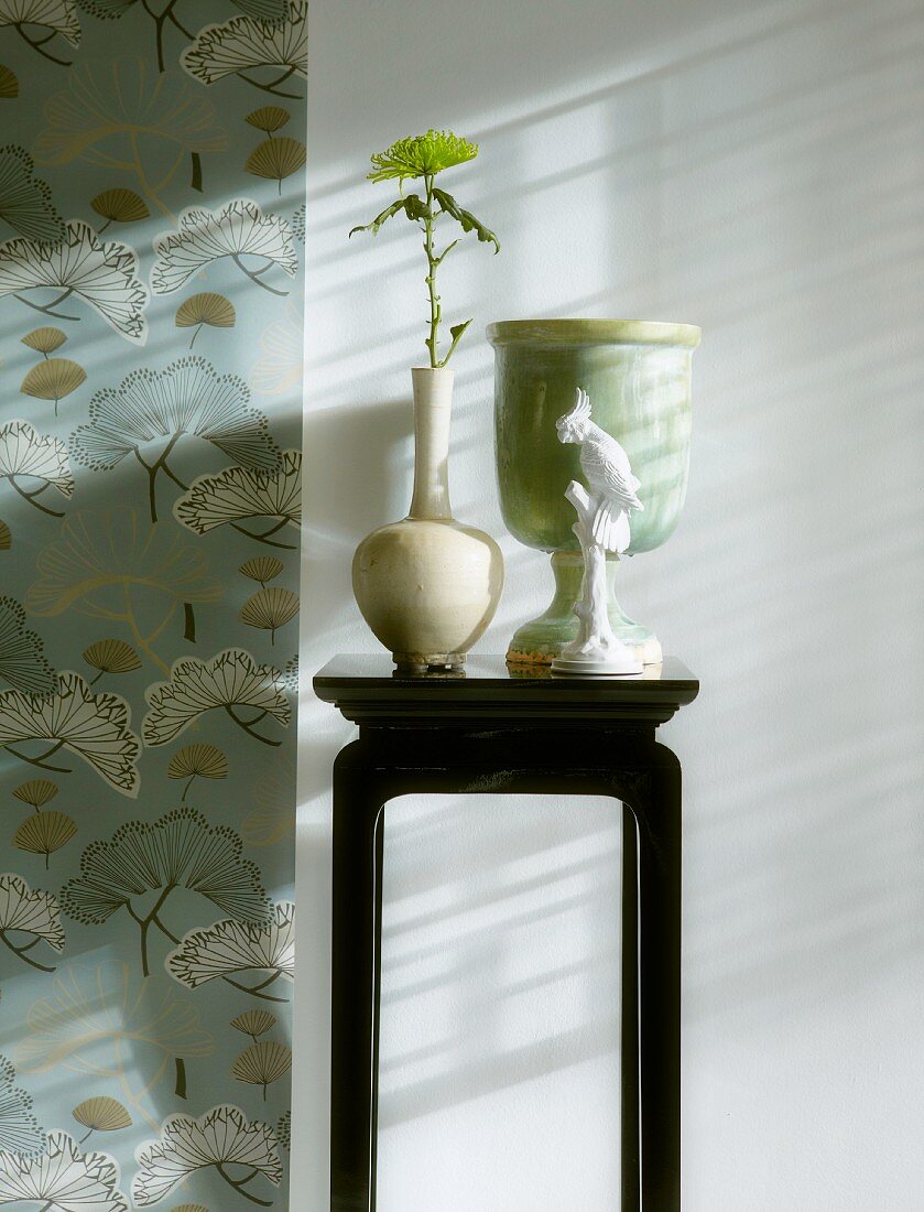 Schwarz lackierter Blumenständer mit Blume in Vase vor Wand neben Tapetenstreifen mit stilisierten Motiven