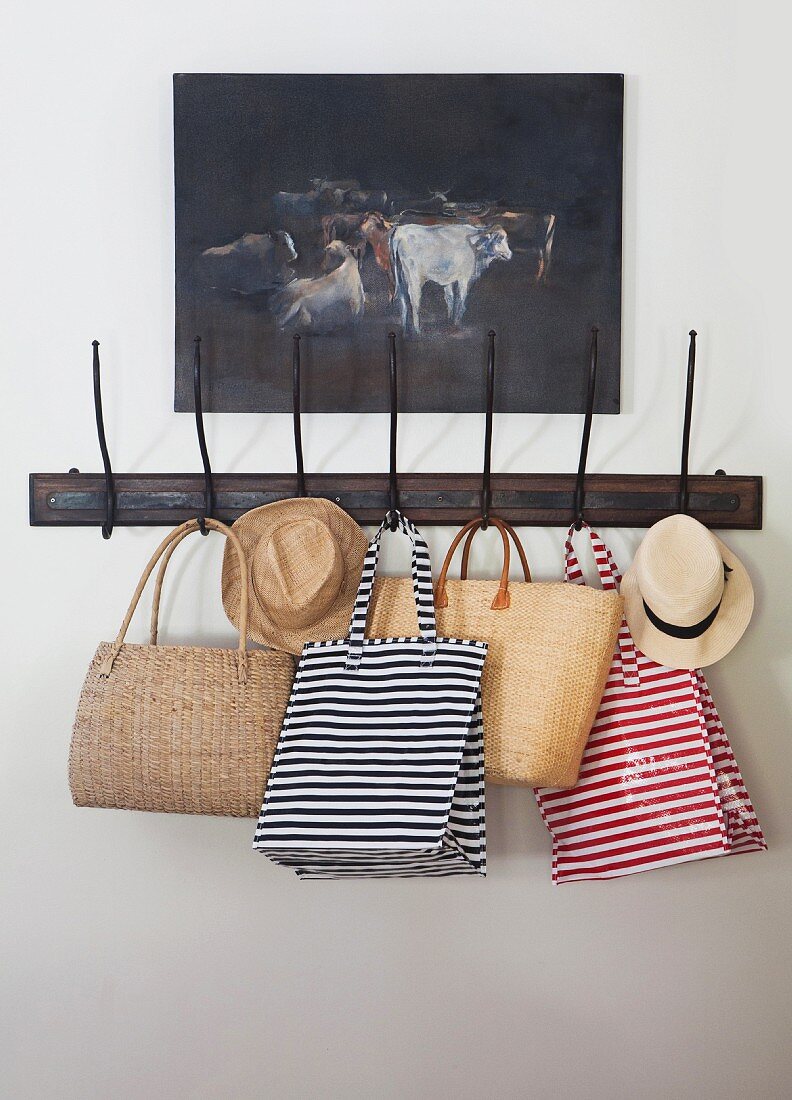 Striped bags and summer hats hanging on vintage coat rack below oil painting of cows