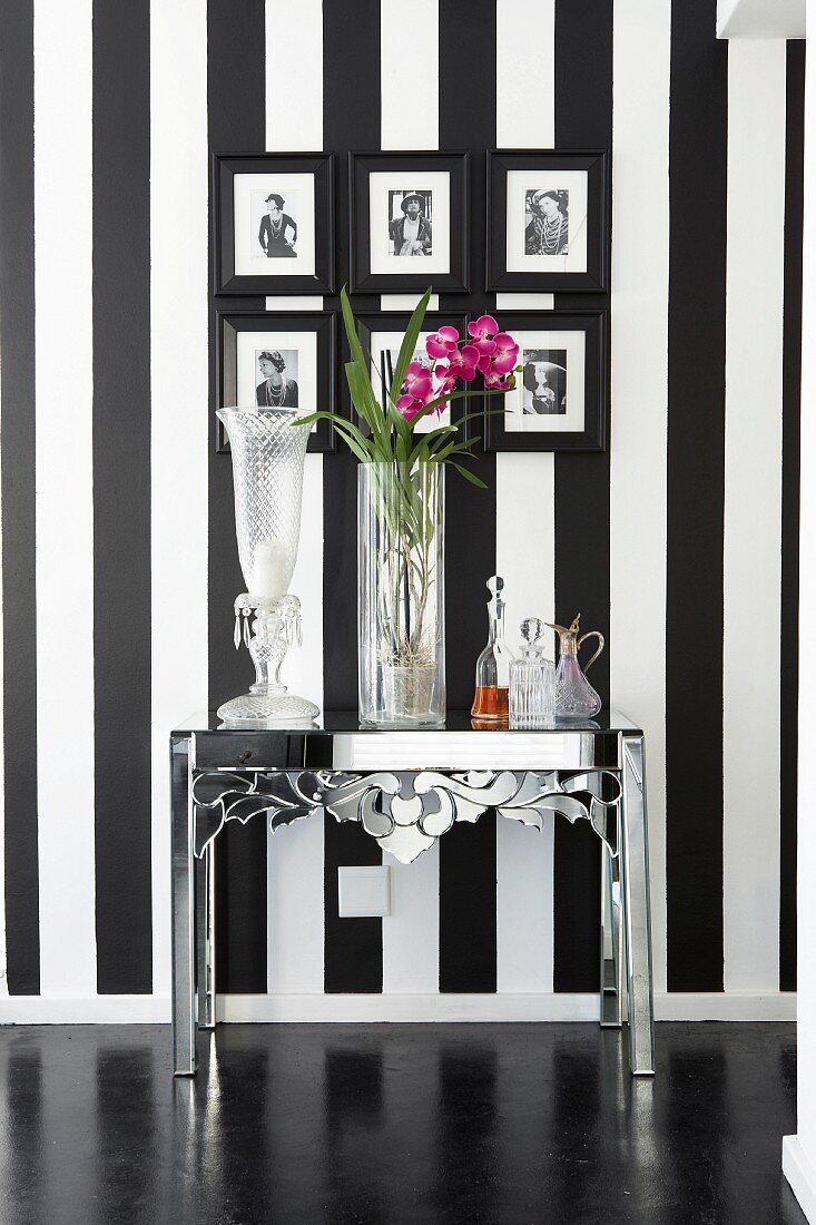 Verchromter Metalltisch mit verschiedenen Blumenvasen vor Wand mit schwarz-weissen Streifen und gerahmter Photogalerie