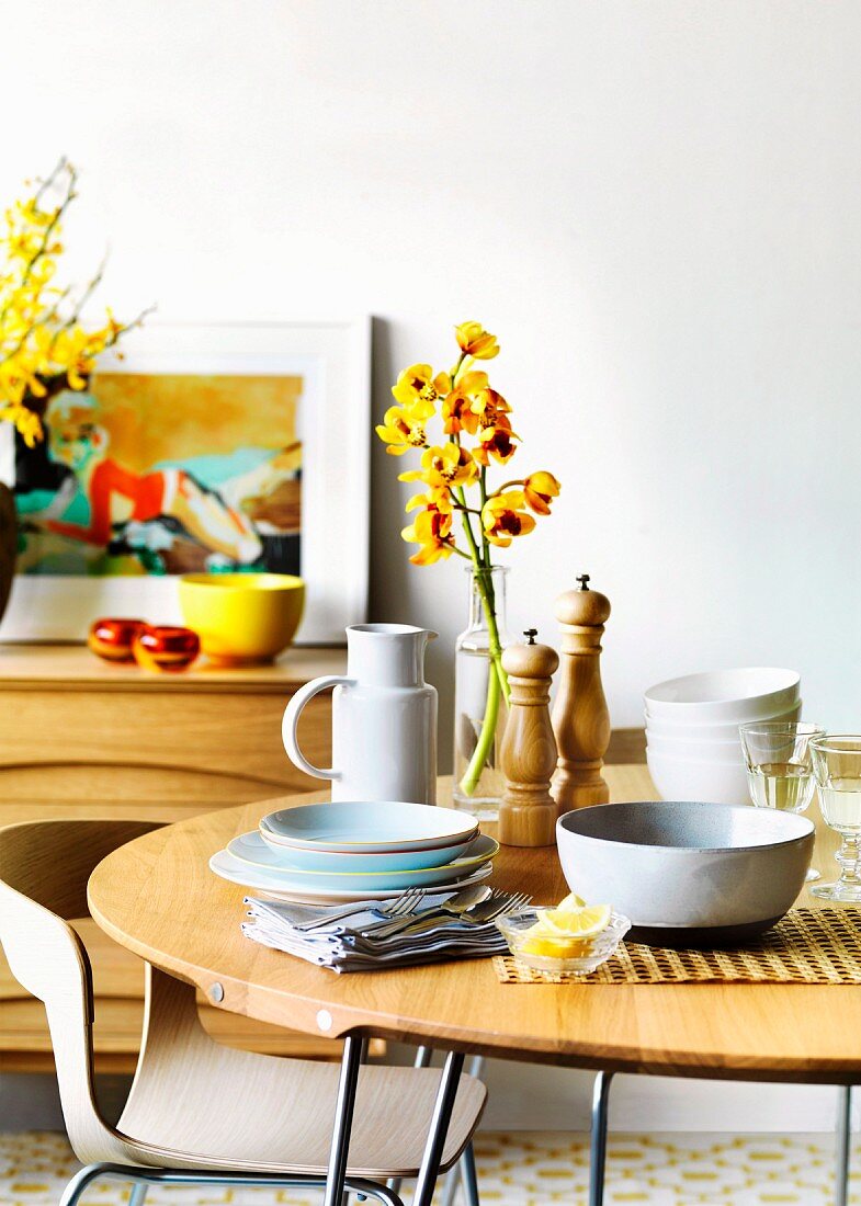 A table laid with crockery, cutlery, salt and pepper grinders and a vase of flowers