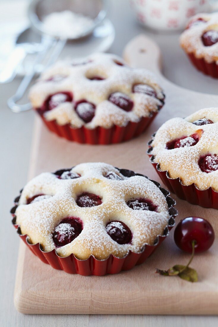 Mini cherry cakes in red baking dishes on a wooden board