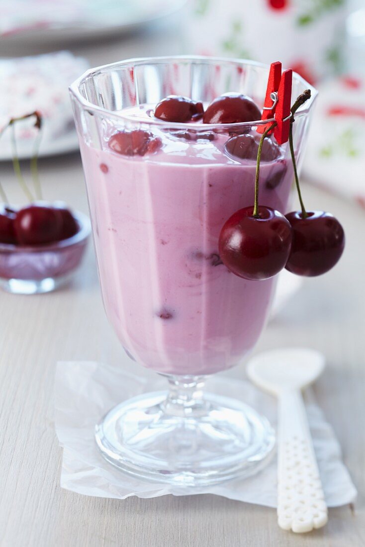 A glass of cherry yogurt garnished with fresh cherries