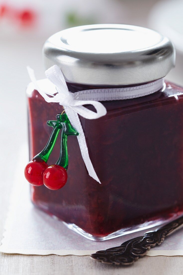 A jar of Cherry jam decorated with a bow and a fake cherry