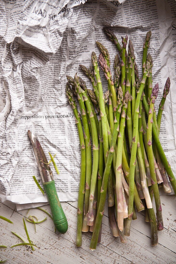 Green asparagus and a peeler on newspaper