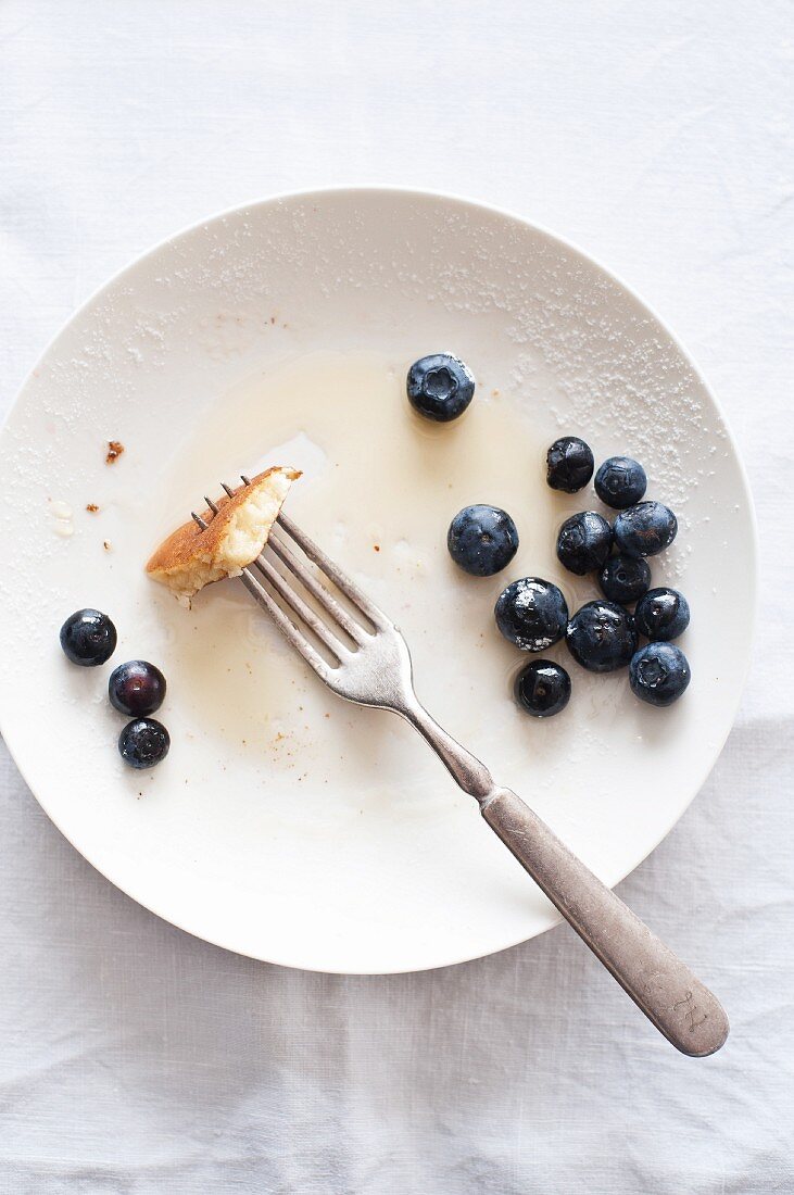 The remains of pancakes with blueberries and maple syrup on a plate with a fork