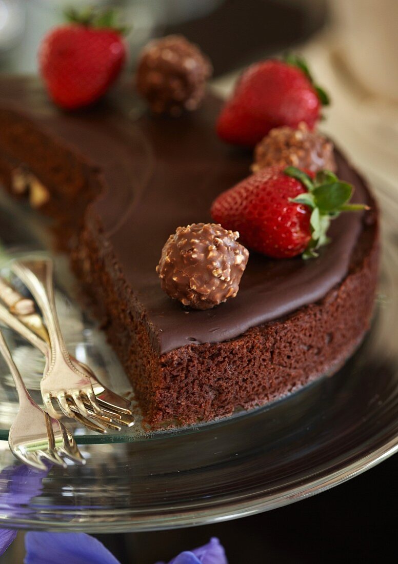 A fine chocolate cake made with cranberries and chocolate ganache and decorated with strawberries and nut pralines