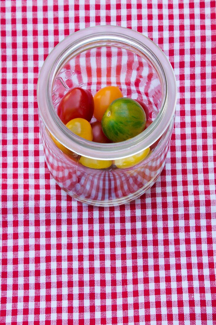 Fresh heirloom tomatoes in a preserving jar on a checked tablecloth