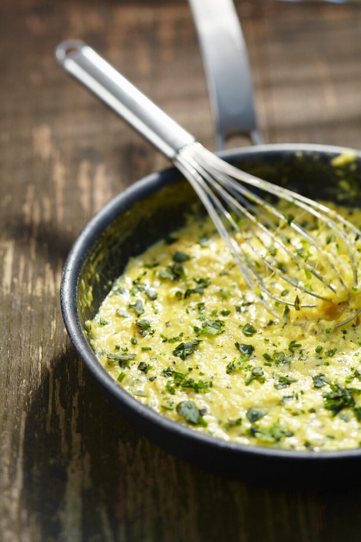 Scrambled egg with herbs in a frying pan