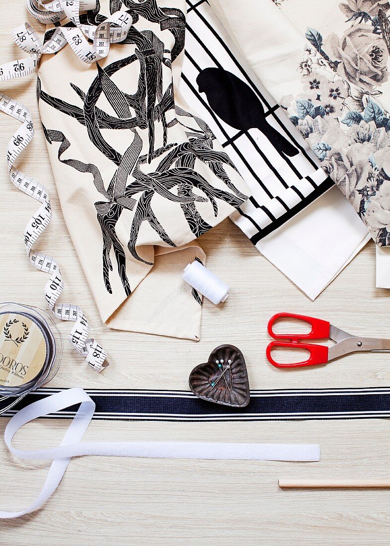 Various tea towels with different patterns, fabric ribbons, scissors, tape measure, spool of thread and pins