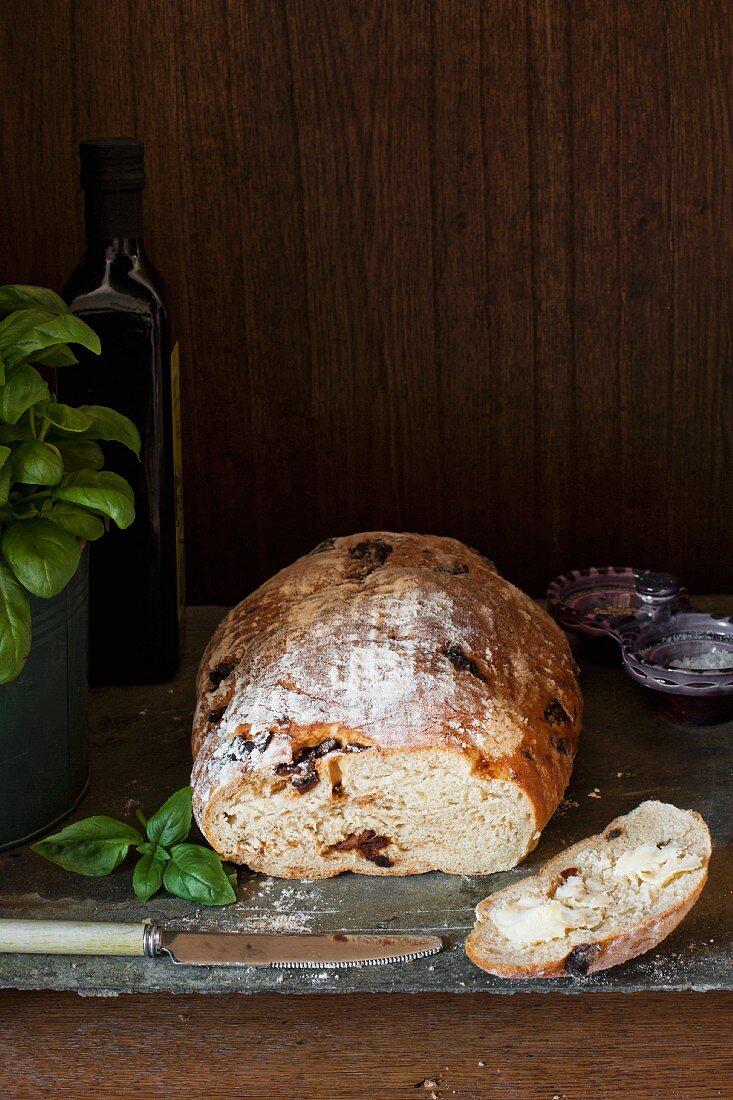 Brot mit getrockneten Tomaten und Basilikum, eine Scheibe davon mit Butter