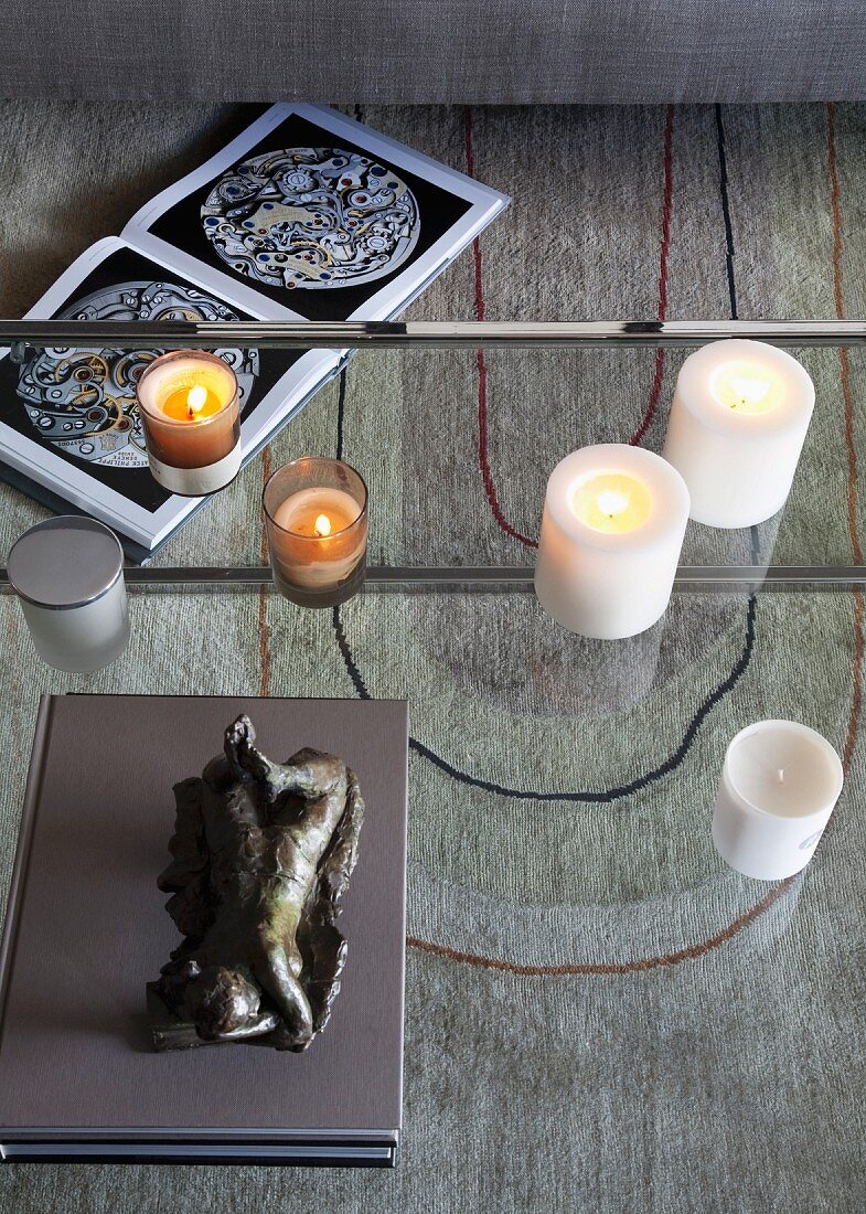 Sculpture and candles on glass table with view of graphic pattern on rug below and open book