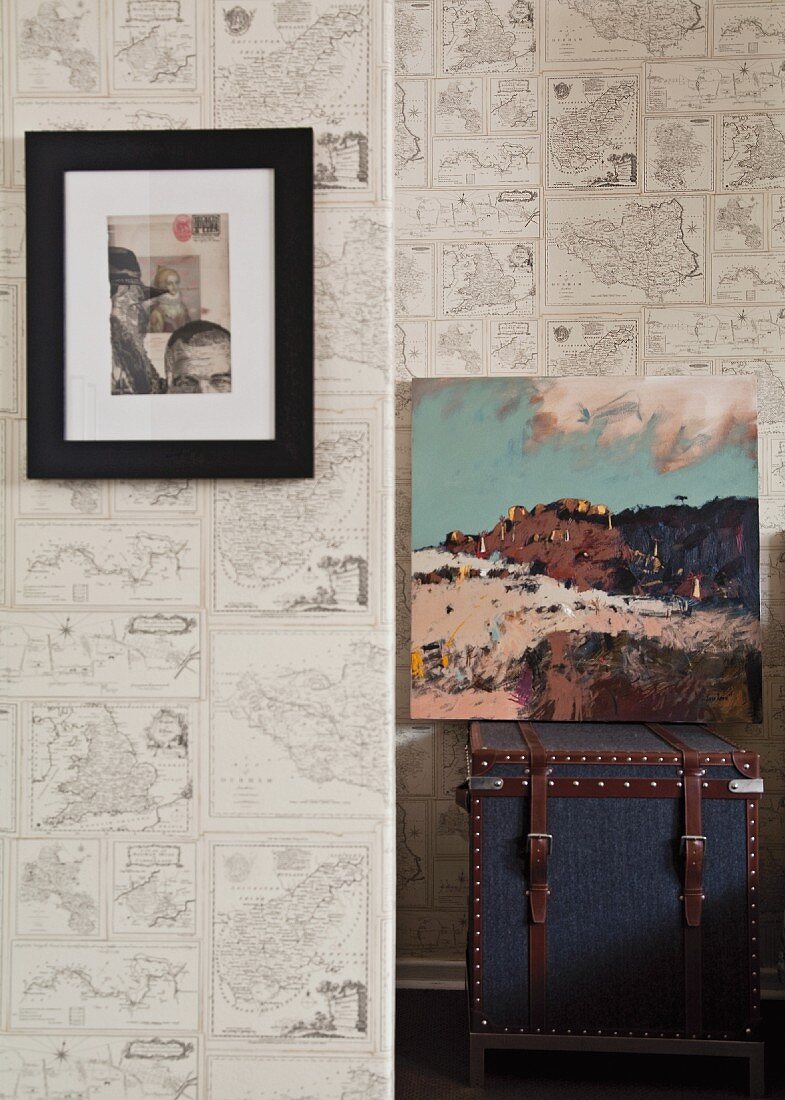 Framed artwork and unframed painting on trunk against wallpaper with pattern of maps
