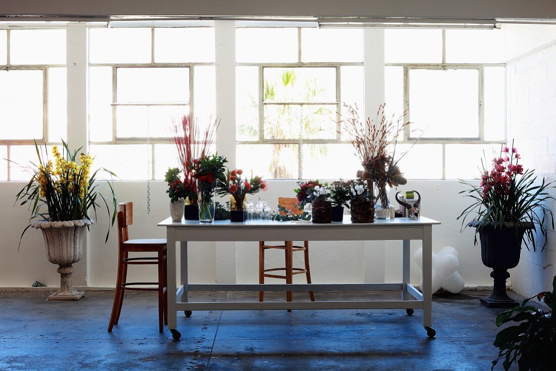 Arbeitstisch eines Floristen mit verschiedenen Blumen und antike Pflanzengefässe vor Fensterband in schlichtem Vorraum