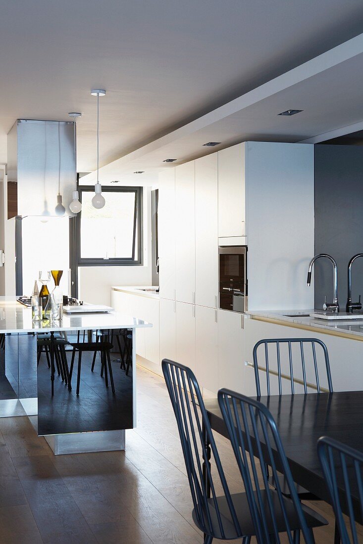 White, designer fitted kitchen with mirrored counter, black dining table and delicate chairs