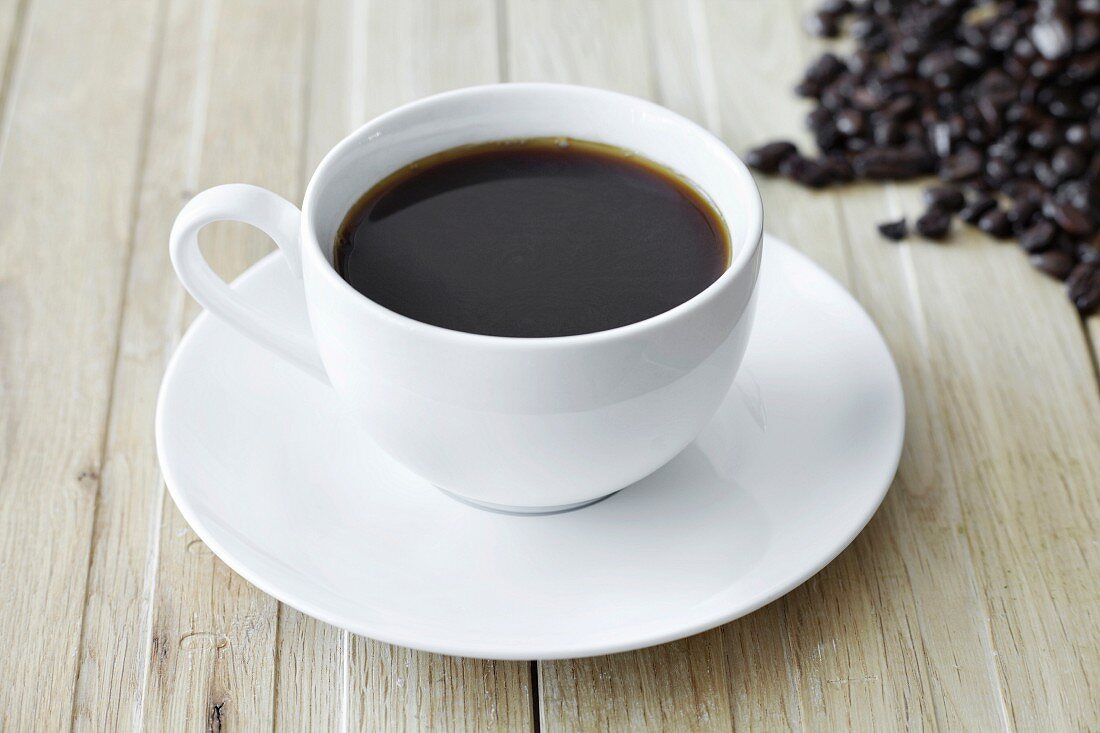 Schwarzer Kaffee in weisser Tasse und Kaffeebohnen