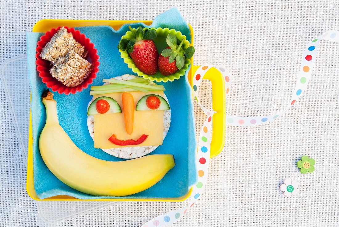 A healthy snack including a face made out of fruit and vegetables