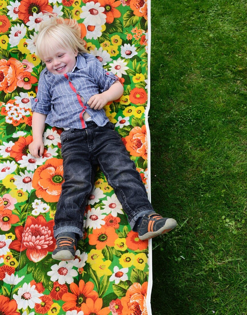 Little boy lying on floral garden lounger (top view)