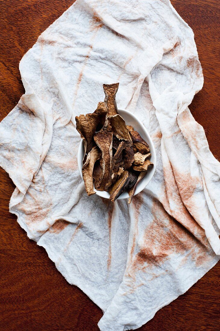 Dried mushrooms in a small bowl on a cloth (view from above)