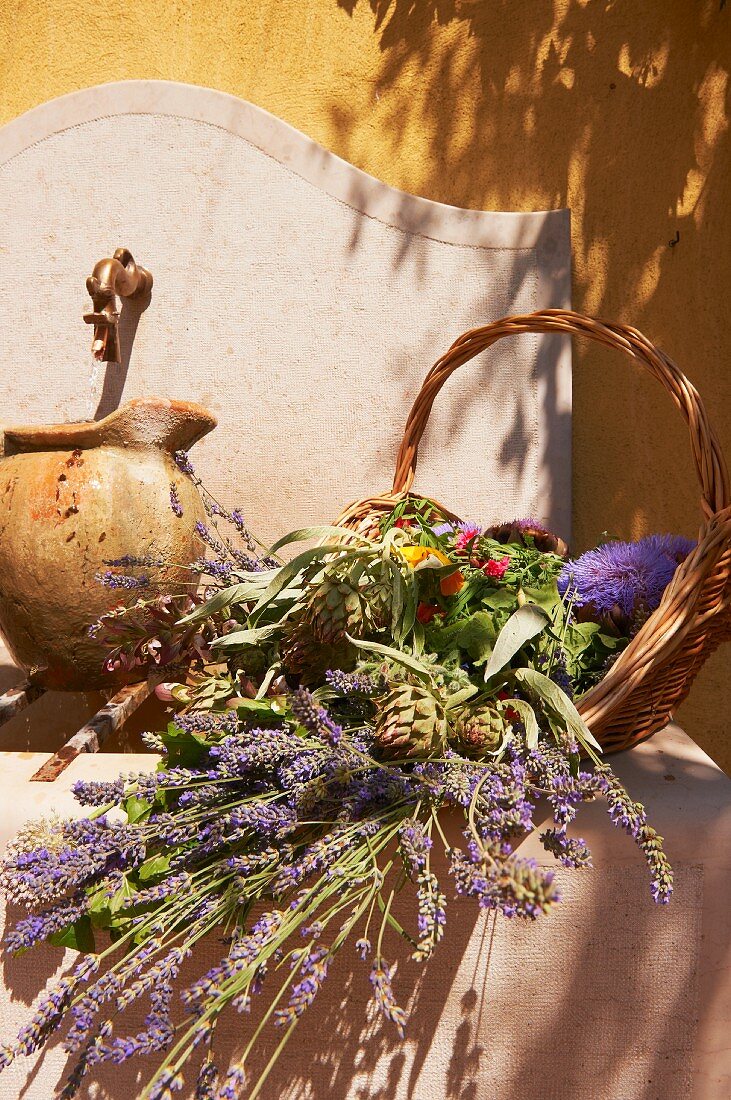 Korb mit Lavendel, Gemüse und Blumen an einem Brunnen in der Provence