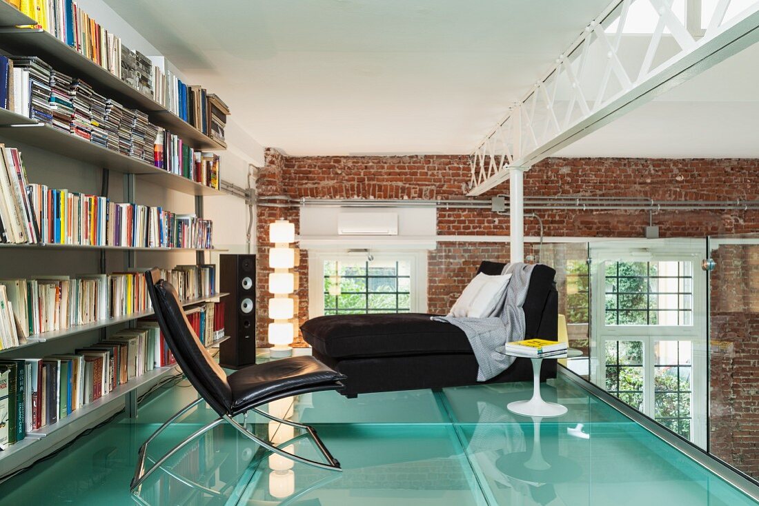 Loft mit weissen Stahlträgern und Backsteinwänden; Ledersessel vor Bücherwand auf einer Schlafgalerie mit Glasboden