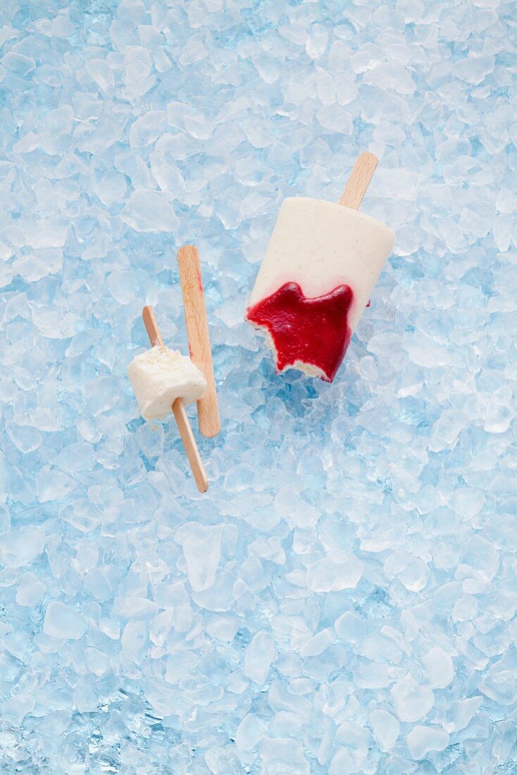 Milk ice lollies with raspberry sauce on crushed ice, partly eaten