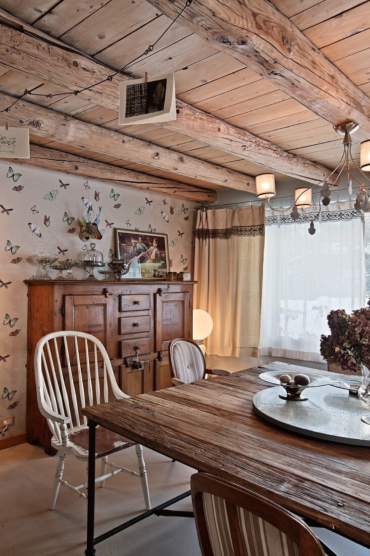 Table with rustic wooden top and vintage chairs in living room with wood-beamed ceiling