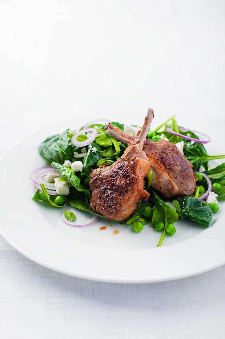 Lamb chops on a spinach salad with peas, onions and feta