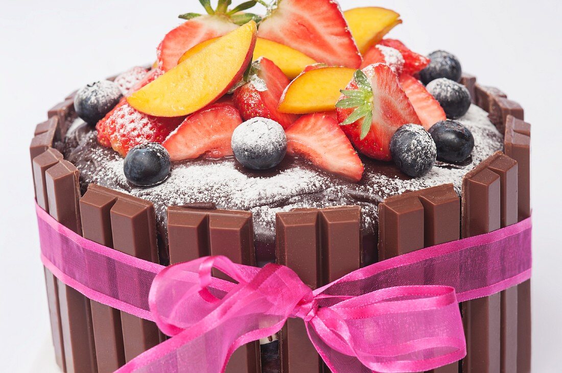 Schokoladentorte mit frischen Früchten, Puderzucker und rosa Schleife