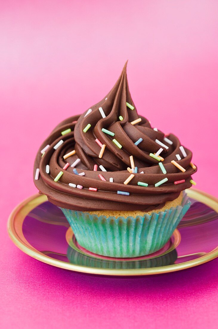 A chocolate cupcake with sugar strands on a pink plate