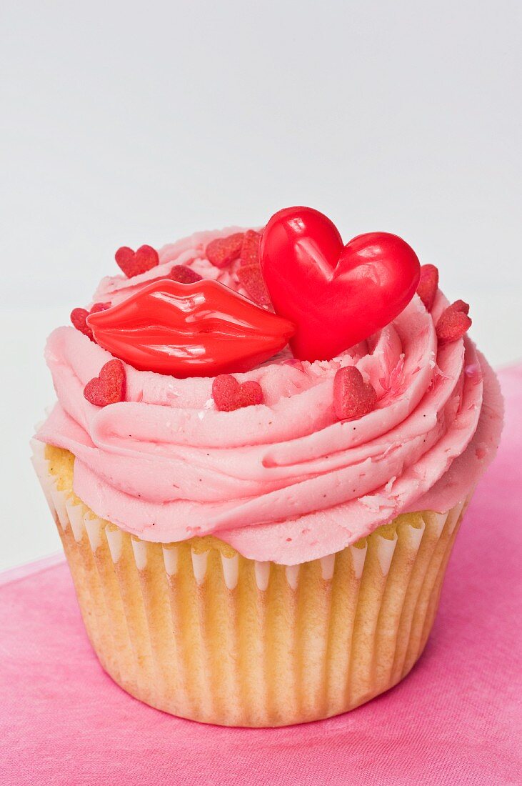 A cupcake topped with pink buttercream icing, red lips and hearts