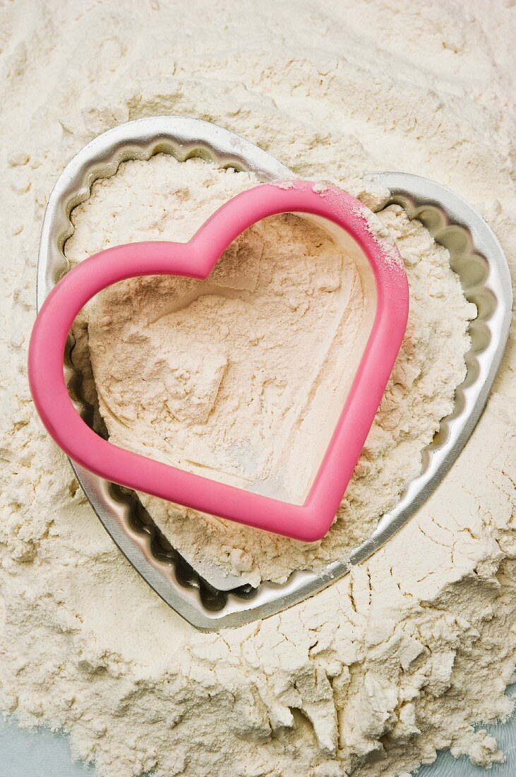 A heart-shaped baking tin and cutter in a mound of flour