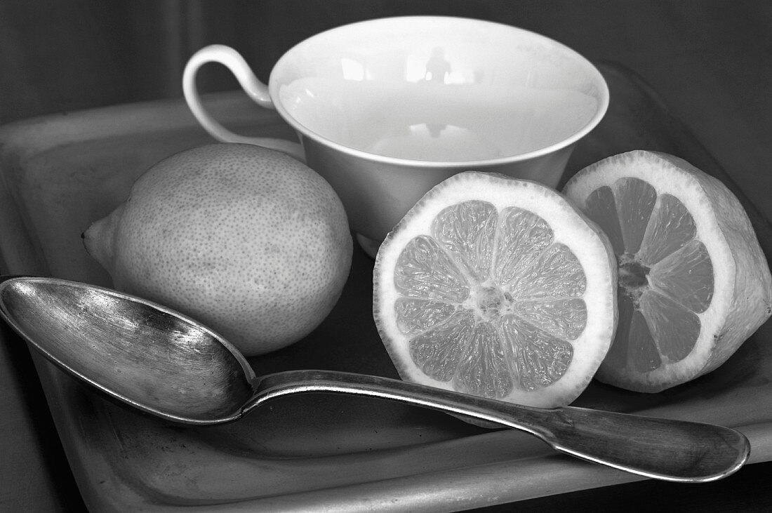 Zitronen und Löffel vor einer Teetasse (Schwarzweissfoto)