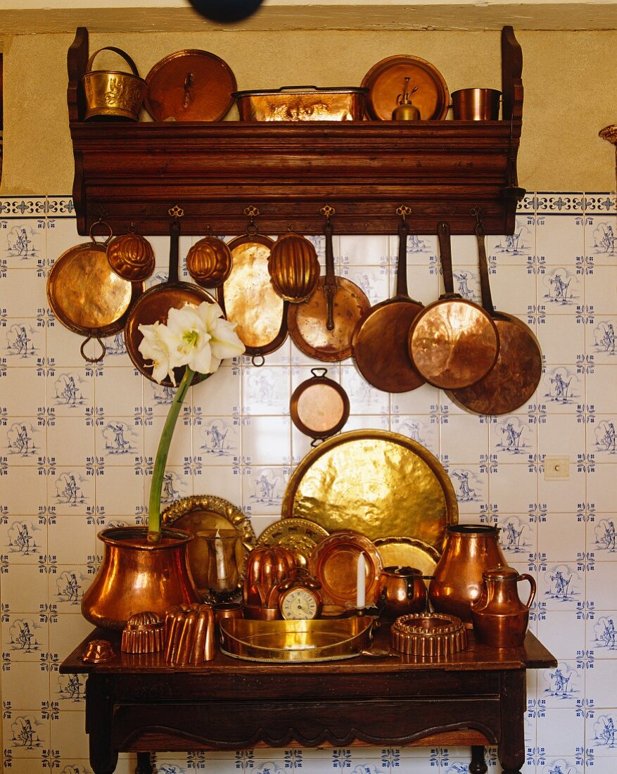 Kupfertöpfe & Kupferpfannen in Regal & auf Holztischchen vor gefliester Küchenwand